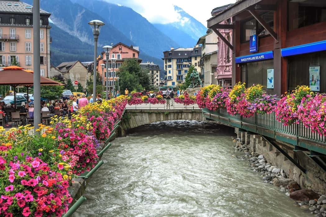 Flower boxes along the Arve in central Chamonix in summer, a footbridge and hotels in front of the mountains