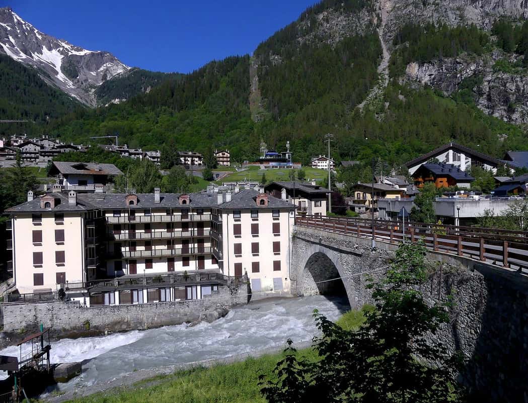 Le hameau de Dolonne à Courmayeur au bord de la Doire Baltée, hôtel et maisons de pierre sous les versants boisés du côté italien