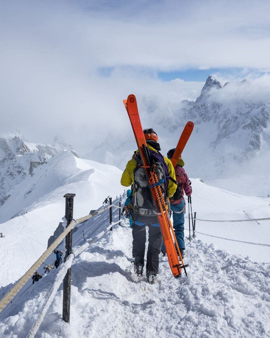Skieurs qui portent leurs skis sur une arête enneigée, au-dessus de la vallée de Chamonix
