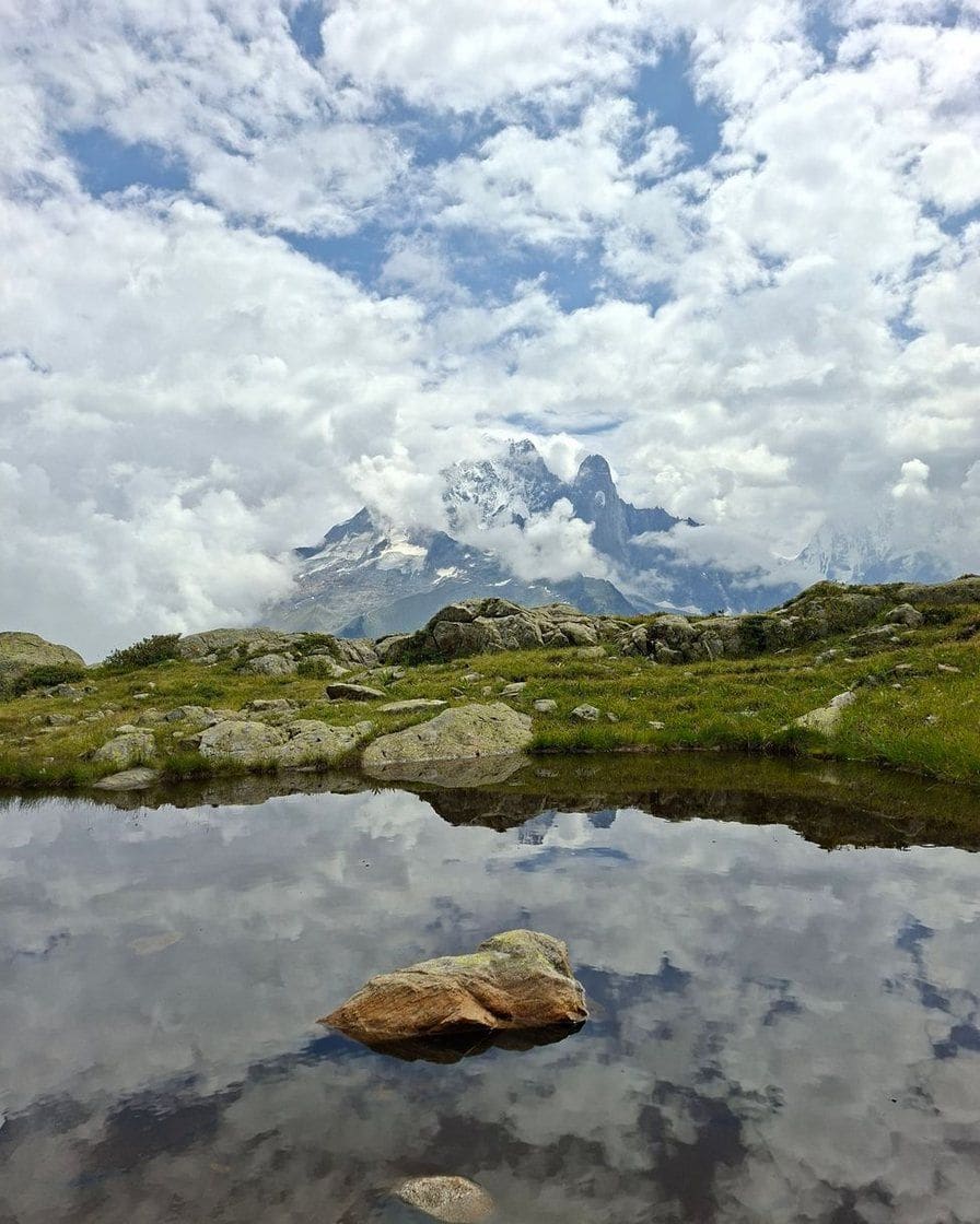 Petit lac d'altitude où se reflètent les nuages, aiguilles du massif au fond