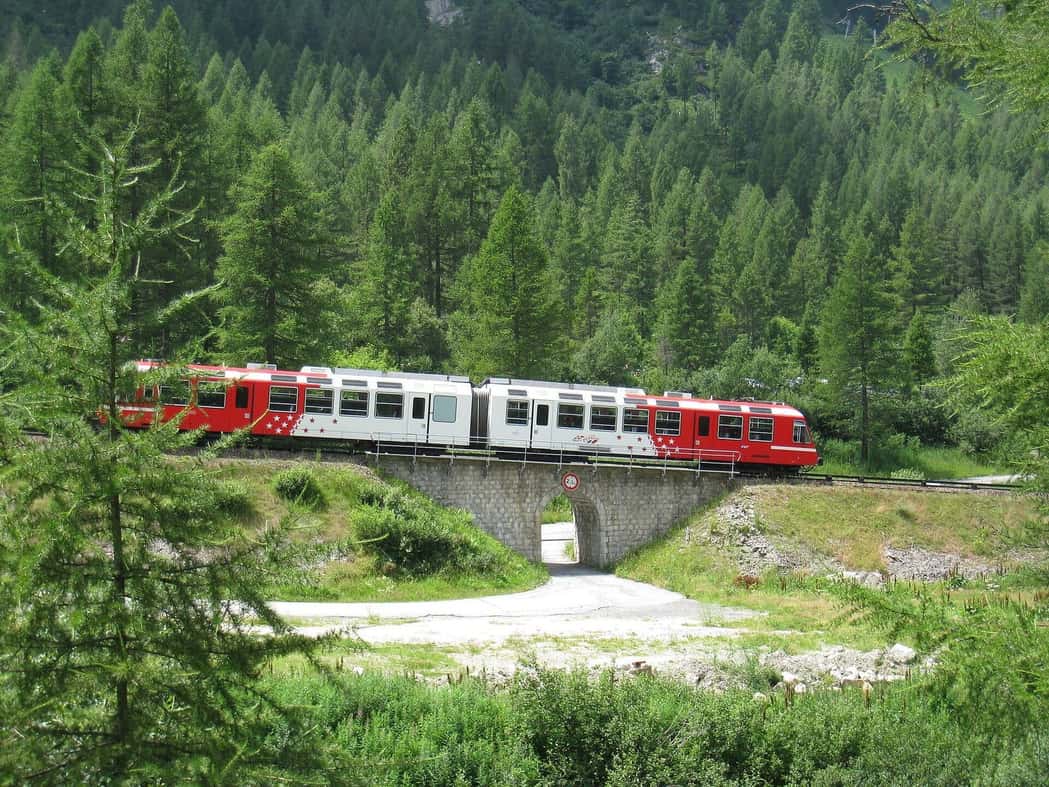 Rame rouge et blanche du Mont-Blanc Express sur un petit viaduc, entre les sapins de la vallée