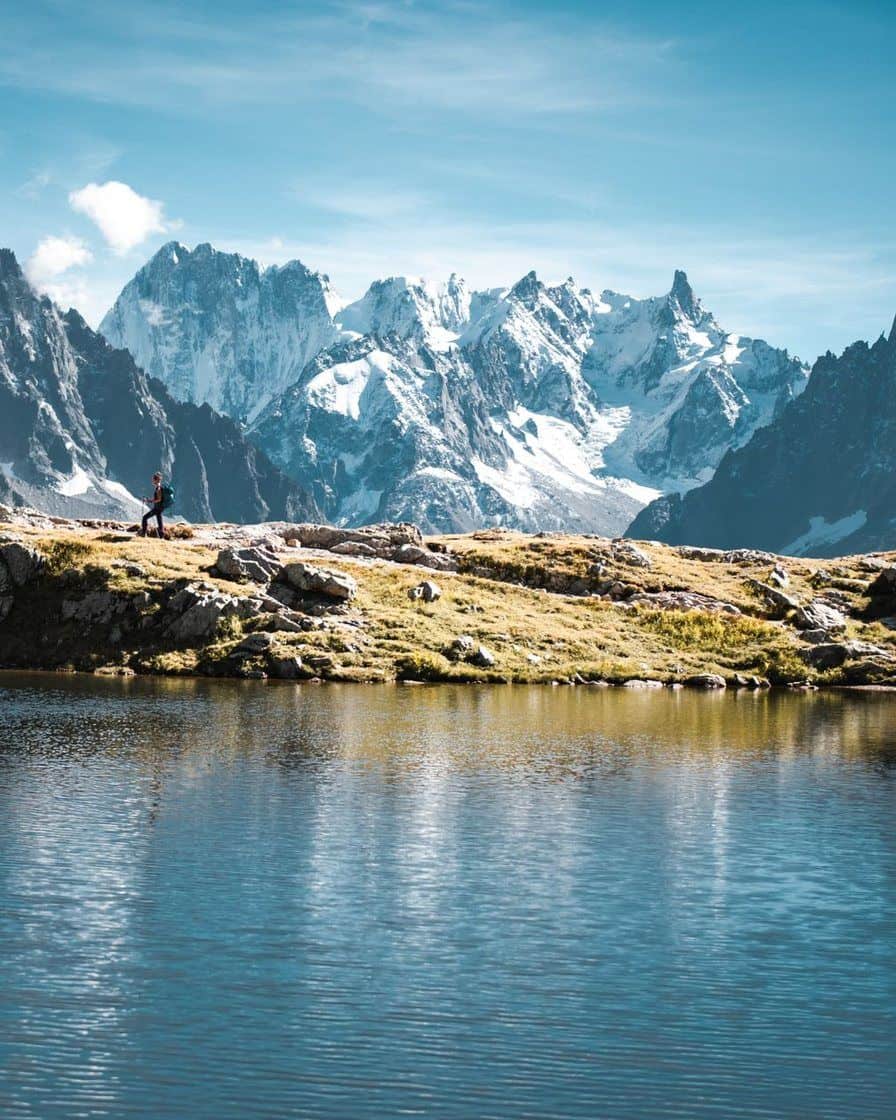 Randonneur au bord d'un lac d'altitude face aux aiguilles enneigées du massif